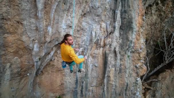 Slow motion of joyful handsome man rock climber hanging on rope and give high five after successful ascent of route on cliff — Stock Video