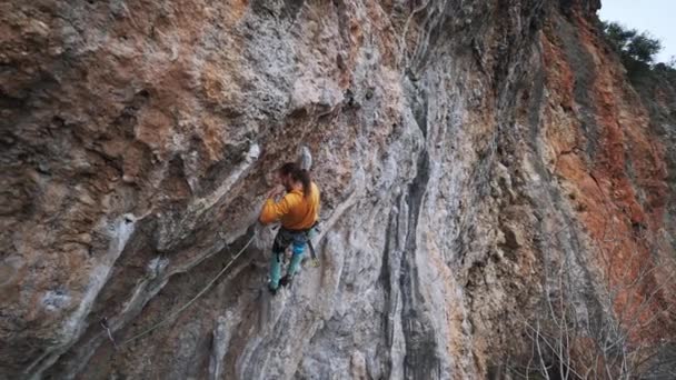 Powolny ruch samiec rock alpinista wiszący na rękę na skalistej ścianie na twardej trasie wyzwanie i przycinanie liny do quickdraw — Wideo stockowe