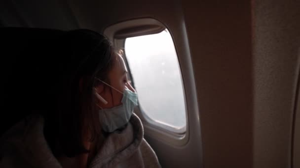 Femme en masque médical de protection dans la cabine de l'avion se trouve à la fenêtre siège et regardant la fenêtre. — Video
