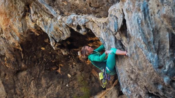 強い女性のロッククライマーは洞窟の中で非常にぶら下がっている黒い崖の上にハードタフな岩のルートを登る. — ストック動画