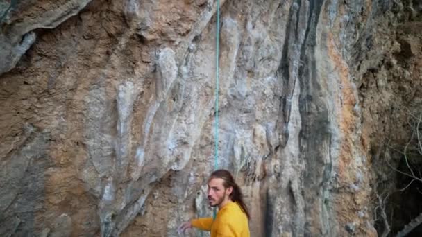 Slow motion of joyful handsome man rock climber hanging on rope and give high five after successful ascent of route on cliff — Stock Video