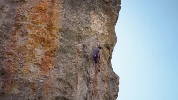 Strong and skillful man climber climbs on limewall cliff by tough route, makes several wide hard efforts and clips rope — Stock Video