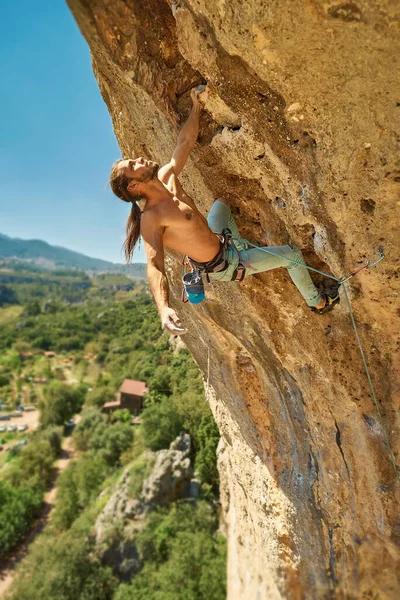 Vahva lihaksikas mies kalliokiipeilijä otteen ja etsivät haastava reitti kalliolla — kuvapankkivalokuva