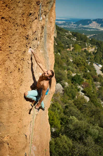 Vahva urheilullinen mies kalliokiipeilijä kiipeily korkealla pystysuoralla kalliolla, luottavaisin mielin reitillä — kuvapankkivalokuva
