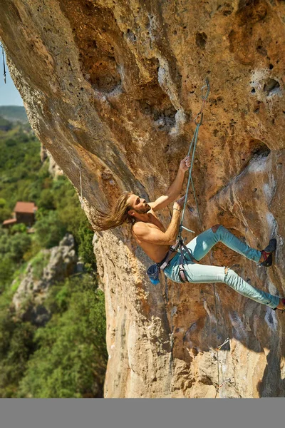 Muskulöser Bergsteiger mit langen Haaren bewegt sich dynamisch auf Klippenfelsen — Stockfoto