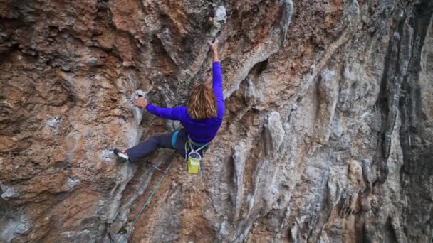 Ağır çekim kadın kayanın tepesine tırmanıyor. Dişi tırmanışçı zorlu rotada tufa tutamını sıkı tutmaya çalışıyor. — Stok video