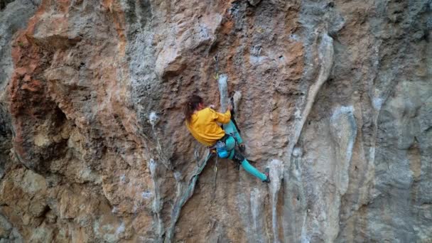 Cámara lenta vista trasera hombre fuerte escalador de rocas sube sobre el peñasco de piedra caliza sobresaliente con colonos. hombre usando barra de rodilla en la pared para descansar y cortar la cuerda — Vídeo de stock