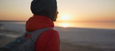 Dikiz manzaralı kadın deniz sahilinde güneşin doğuşunu seyrediyor altın güneş ışığı altında manzaranın tadını çıkarıyor.