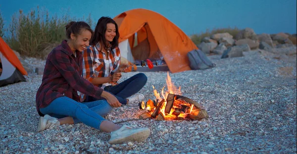 Esbo pari paahtamalla vihanneksia tulessa, istuu rannalla vieressä teltta camping. — kuvapankkivalokuva