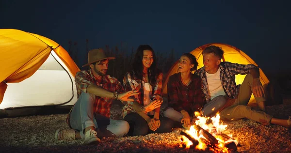 Ystävät rentouttava, lämpeneminen ja hauskaa kokko telttailu telttoja everning — kuvapankkivalokuva