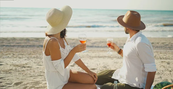 Tyylikäs pari istuu rannalla, nauttii merinäköalasta ja juo viiniä — kuvapankkivalokuva