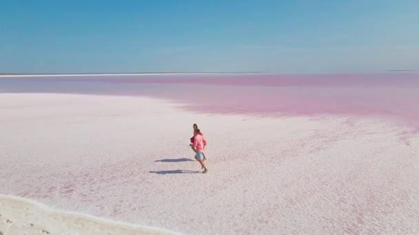 분홍색 옷을 입은 행복 한 젊은 부부가 밝은 색깔의 분홍빛 광물 호수가 있는 하얀 해안에서 즐겁게 즐겁게 뛰노는 장면 이 공중에서 촬영되었다 — 비디오