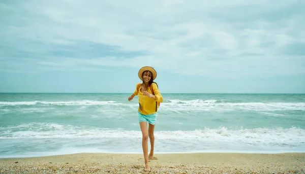 Glückliche unbeschwerte Frau mit Hut, die aus dem Meerwasser rennt und am Strand genießt, — Stockfoto