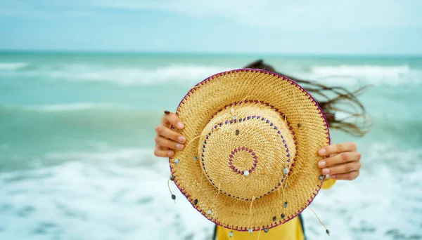 Kvinne med sommerstråhatt foran kamera på vindfylt strand – stockfoto