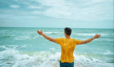 Arkadan bakan özgürlük adamı kollarını açmış güzel deniz manzarasının önünde duruyor.