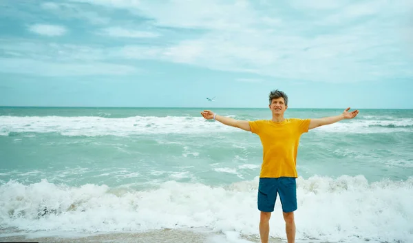Muotokuva iloinen onnellinen mies keltaisessa paidassa avosylin nauttia lomista rannalla — kuvapankkivalokuva