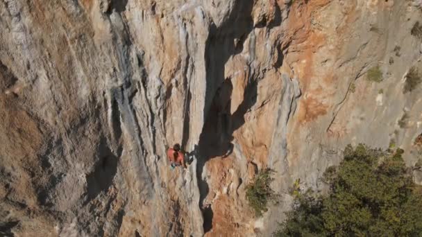 Luftaufnahme von der Drohne eines kräftigen, muskulösen jungen Mannes, der am Seil hängt und nach dem Klettern auf einem hohen Felsen durch eine herausfordernde Kletterroute abstürzt. — Stockvideo