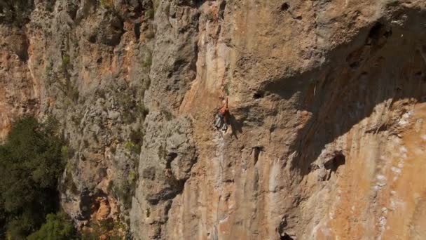 Letecký pohled z dronu silného svalnatého mladíka zavěšeného na laně a sestupujícího po lezení na vysokém útesu náročnou horolezeckou cestou. — Stock video