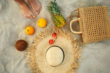 Moda kıyafetlerinin yanında yaz kadınlarının ayakları ve kumun üzerinde yatan tropikal meyve düzlüğü.