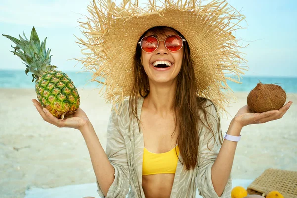 Lykkelige smilende kvinner i røde briller med stråhatt på stranden, som holder tropiske frukter i sine hender, jenter som ser glade ut på sommerferie. piknik ved sjøen – stockfoto