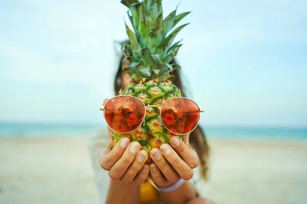 Lähikuva naisten kädet pitämällä hauska nukke pään ananas vaaleanpunainen aurinkolasit ja näyttää sen kameralle. — kuvapankkivalokuva