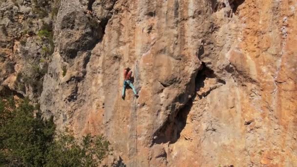 Luchtfoto van drone van sterke gespierde jongeman klimt op grote rotsachtige muur door uitdagende rotsklimroute. — Stockvideo