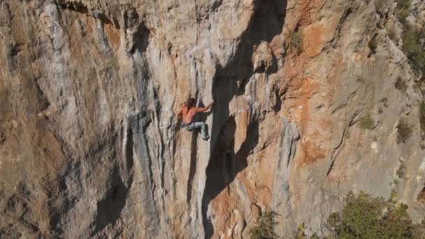 Letecké drone záběry silného svalnatého muže lezení náročné skalní horolezecké trasy na svislém útesu s obrovským tufou. horolezec dělá dlouhý tvrdý pohyb, selhává a padá — Stock video