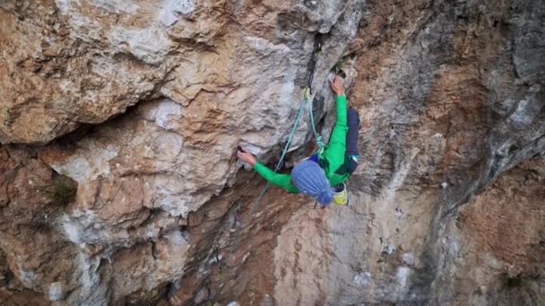 Lassított légi felvétel erős moman sziklamászó mászik overhanging crag kemény kihívást jelentő útvonalon. nő tesz kemény erőfeszítést, és eléri tartja a lábát — Stock videók