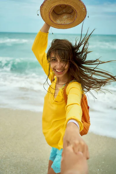 Porträt einer glücklichen Frau mit wehenden Haaren, die am Strand Spaß hat und jemanden an der Hand hält — Stockfoto