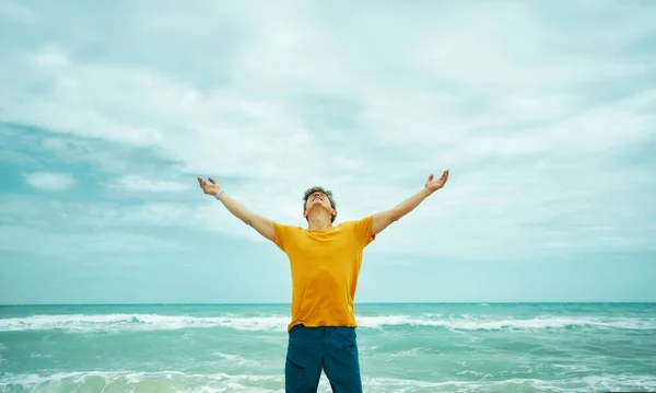 Inspirierter Mann genießt majestätische Meereslandschaft beim Blick nach oben und erhobene Hände — Stockfoto