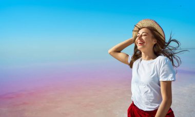 Parlak bir portre, parlak pembe göl üzerinde şapkalı bir kadın, mavi gökyüzü, renkli doğa manzarası.