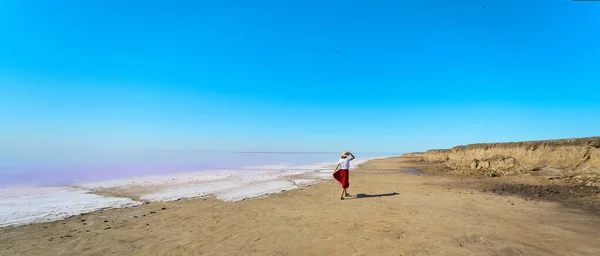 Panoraama kuva kaunis maisema, nainen kävelee rannalla lähellä suolaa vaaleanpunainen järvi — kuvapankkivalokuva