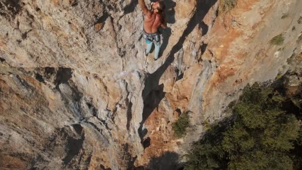 Letecký pohled z dronu silného svalnatého muže stoupá náročnou horolezeckou trasou. horolezec dosáhne držadla a dělá dlouhý tvrdý pohyb — Stock video
