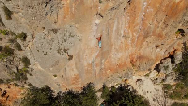 Luchtfoto van drone van sterke gespierde jongeman klimt op grote rotsachtige muur door uitdagende rotsklimroute. — Stockvideo