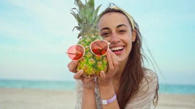 Sahilde kırmızı güneş gözlüklü ananas tutan gülen kadın.