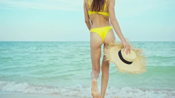 Sexy bikini cuerpo mujer caminando en la playa de arena, sosteniendo sombrero de paja en vacaciones de viaje — Vídeo de stock