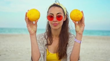 Yazlık giysiler giymiş, gözlerinde meyve tutan komik, neşeli genç bir kadın.