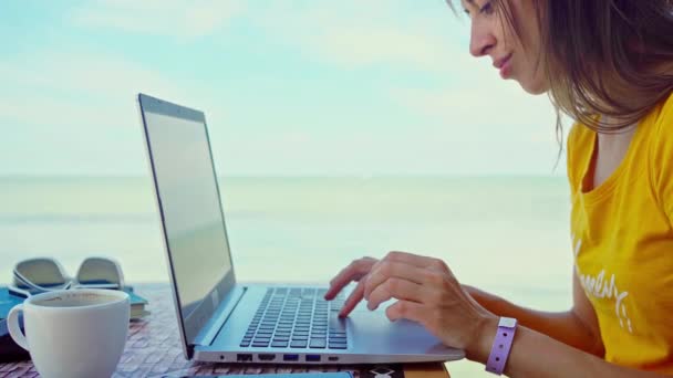 Συγκεντρωμένη γυναίκα που εργάζεται σε εξωτερικούς χώρους κοντά στη γαλάζια θάλασσα σε φορητό υπολογιστή — Αρχείο Βίντεο