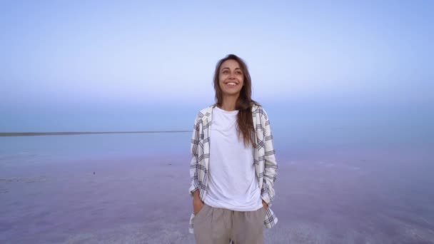 Camera zooming in to Happy smiling woman enjoying sunset at nature landscape at pink salt lake at evening — Stock Video