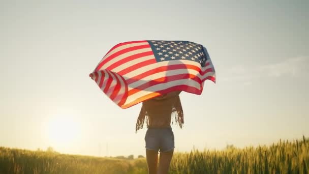Zeitlupe Schöne Frau, die bei Sonnenuntergang mit einer USA-Flagge im Freien spaziert — Stockvideo