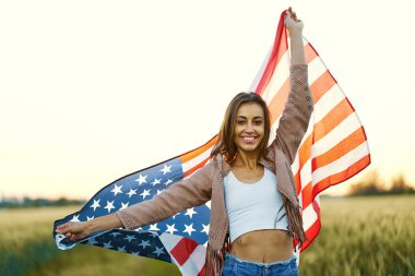 Gün batımında sahada yıldız ve çizgiler sallayan kendine güvenen bir kadın. Bağımsızlık Günü