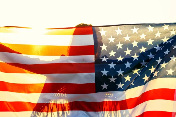 Menina silhueta segurando estrelas americanas e listras bandeira, de pé em sol de verão — Fotografia de Stock