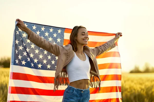 Libertà americana donna a braccia aperte con bandiera americana al tramonto dorato campo — Foto Stock