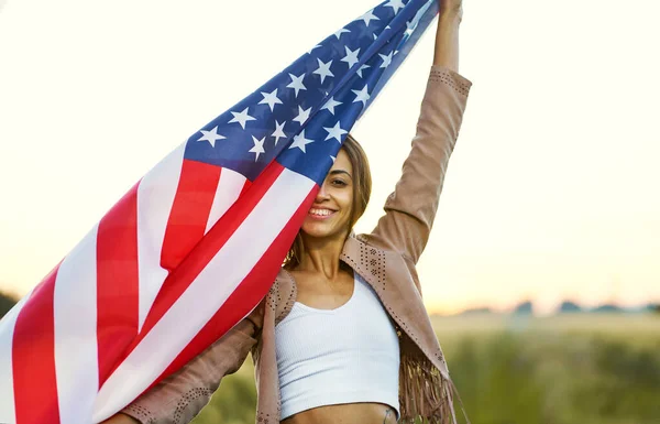 En positiv kvinne som dekker halve ansiktet med amerikansk flagg på banen. USA feirer 4. juli – stockfoto