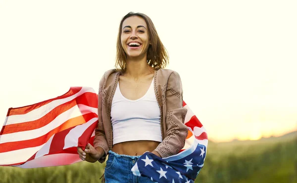 Laughing girl enjoying nature at sunset in summer, running at field with American flag — Stock Photo, Image