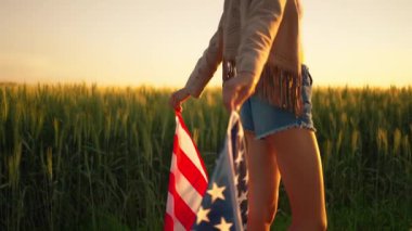 Gün batımında ellerini kaldırıp Amerikan bayrağını tutan mutlu bir kadın.