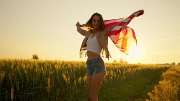 American freedom woman with open arms holding american flag at golden sunset field — Stock Video