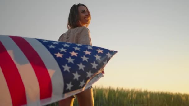 4 de Julho. Mulher americana com a bandeira nacional americana contra belo marco no pôr do sol — Vídeo de Stock