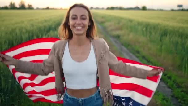 Lachend meisje genieten van de natuur bij zonsondergang in de zomer, hardlopen op het veld met Amerikaanse vlag — Stockvideo