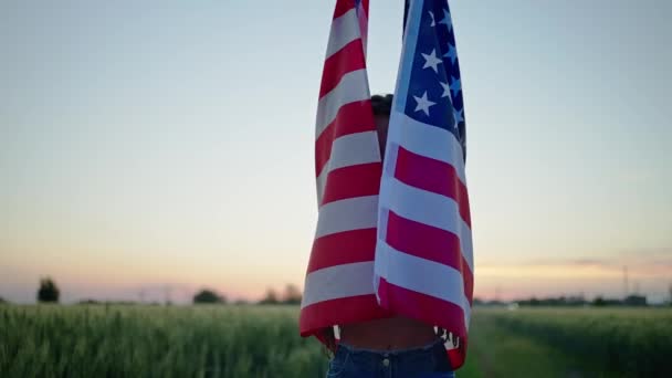 Cheerful young woman wrapped in United States flag outdoors with polica lights on face. — Stock Video